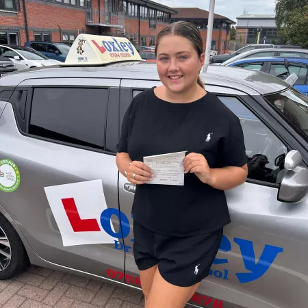 A young woman stands by a learner car, showing that she passed her driver's license.