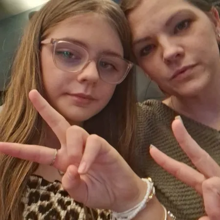 A mother and daughter pose with peace signs in a selfie.