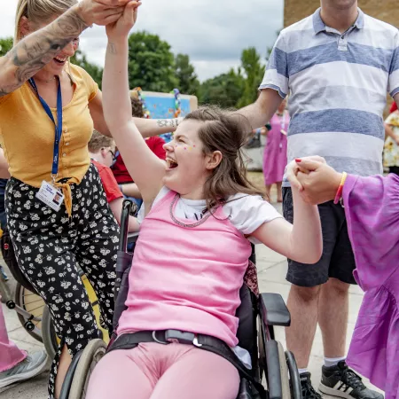 A young woman in a wheelchair celebrates an accomplishment, surrounded by a crowd.