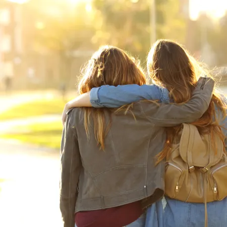 Two female friends stand arm in arm.