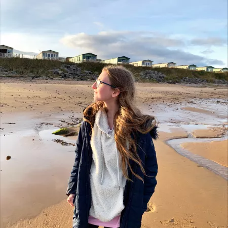 A young woman looks into the sun on a beach.