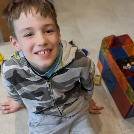 A boy smiles beside his toy blocks.