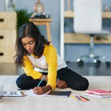 A teenager, sat on the floor, writes notes down in a diary.