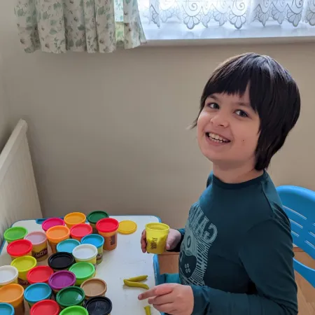 A young boy smiles at a desk laden with colourful play doughs.