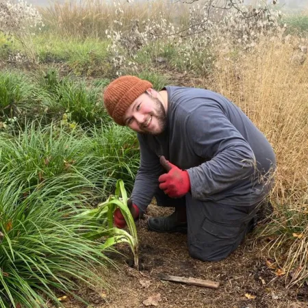 A young man smiles as he tends his garden.