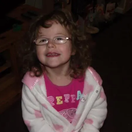 Young girl wearing glasses smiling to camera wearing pink pyjamas.