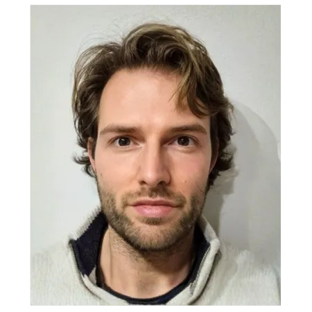 man with short wavy brown hair in a beige top