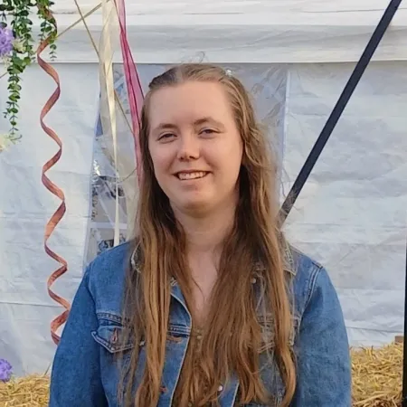 A young woman with long hair and a denim jacket smiles. 
