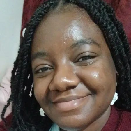 A young woman with braids smiles to camera.