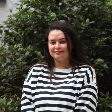 A young woman in a striped shirt smiles outside.