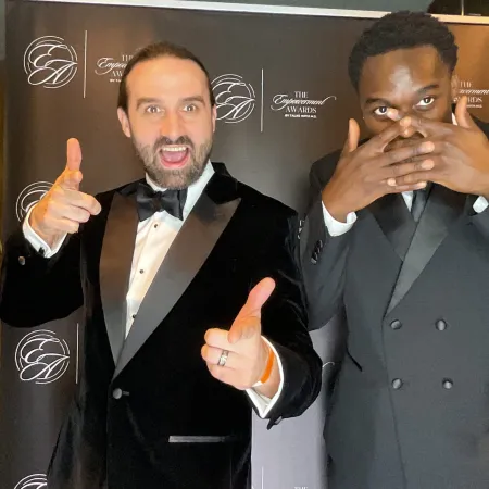 Two young men in suits stand at the step-and-repeat at the Empowerment Awards.