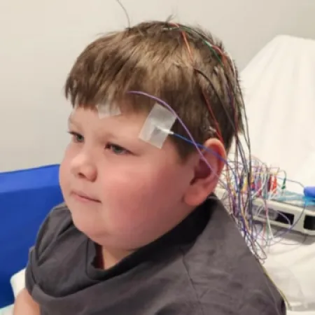 A boy sits in a hospital bed with an EEG.