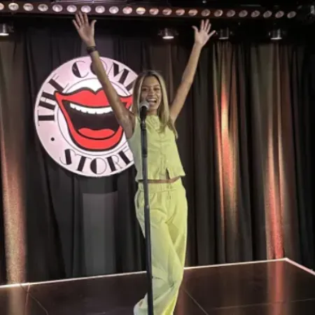 A woman raises her arms above her head on the Comedy Store's stage.