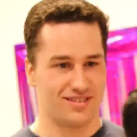 A close-up shows a young man smiles against a pink background.