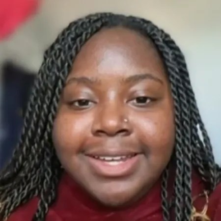 A young woman with braids smiles to camera.