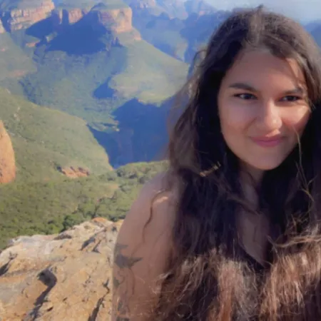 A young woman stands overlooking rocky mountains and a forested valley.