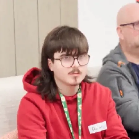 A young man in glasses sits wearing a lanyard. 