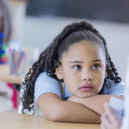 A young girl sits thoughtfully at a desk.
