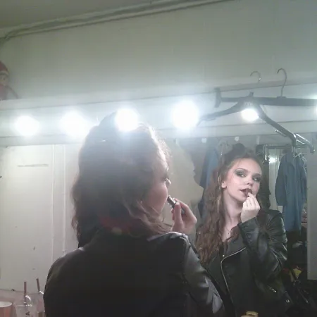 A young woman applies theatrical makeup.