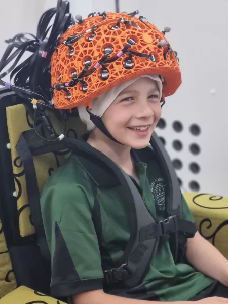 Young boy smiles at camera wearing an orange OPM-MEG helmet