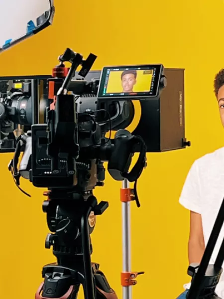 Photograph of young boy being interviewed to camera.  The view is from behind the camera.  The set is yellow and you can see the boys face in the camera's view.