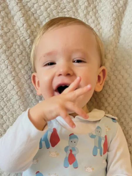A young boy who lives with epilepsy smiles and gestures from his bed.