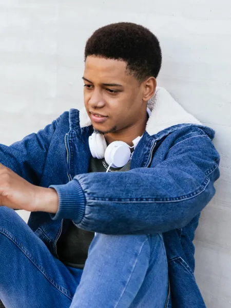 A young person concentrating on his mobile phone with headphones around his neck.