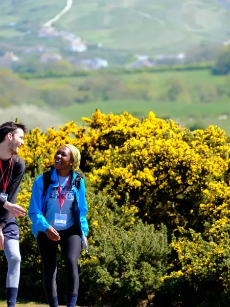 A man and women chatting and walking in front of yellow bushes 