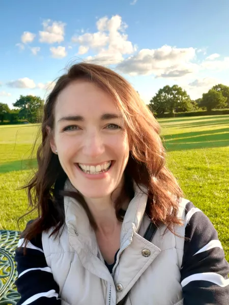 A young woman smiles in a selfie in front of a sunlit field.