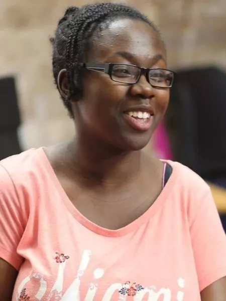 A young woman wearing a pink t-shirt and glasses smiles off camera.