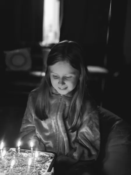 A girl, depicted in black and white, blows out birthday candles.