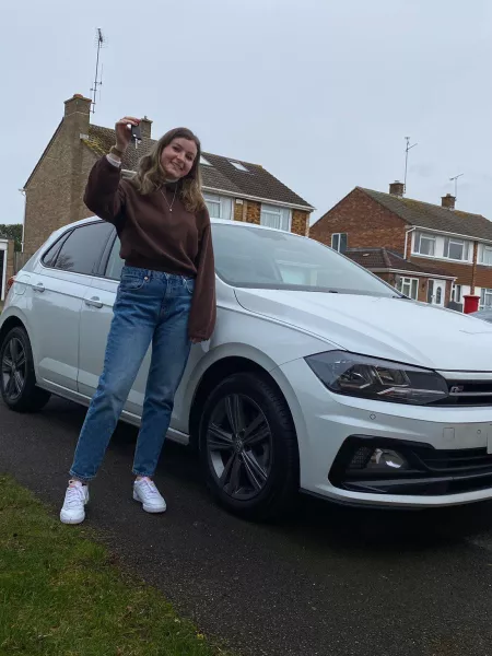 Young woman stands by a car and holds up her car keys.