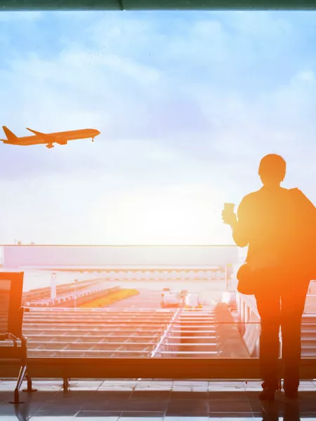 A person watches a plane take off from an airport boarding gate.