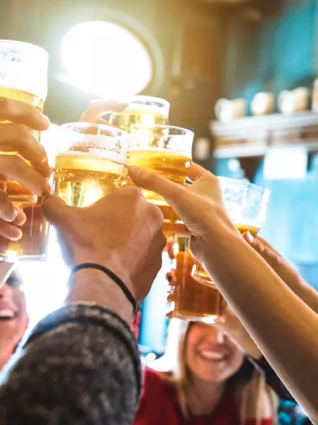 A group of young people cheers with pints of beer in a bar.