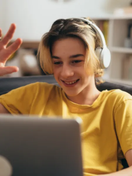 A teenage boy smiles and waves on a video call.