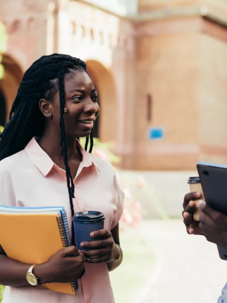 Young male and female adults chat with notebook and coffee in hand.