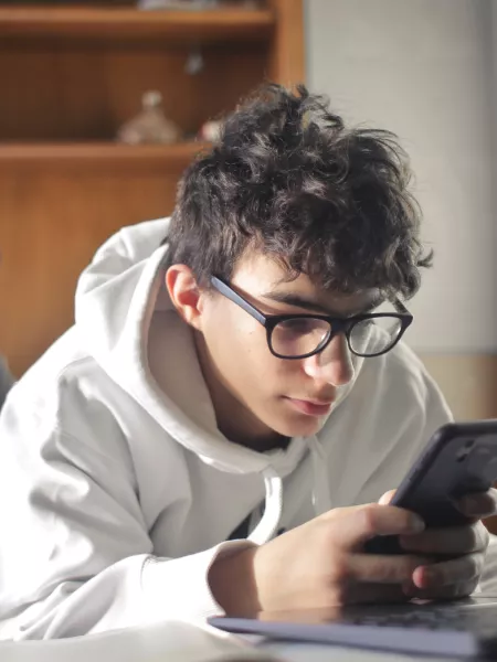 Young boy lying on his bed looking at his phone and laptop