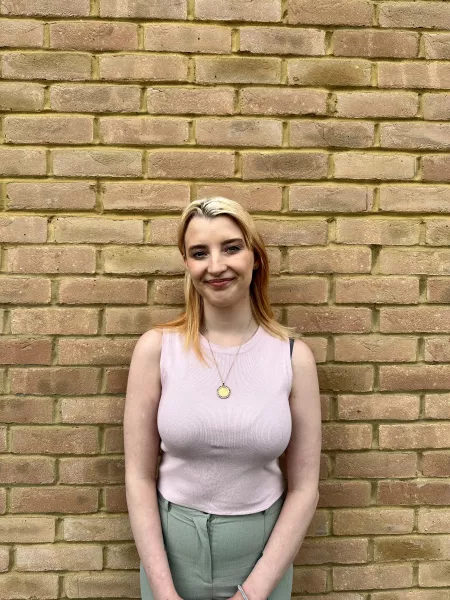 Bethany, a young blonde woman, stands smiling against a brick wall.