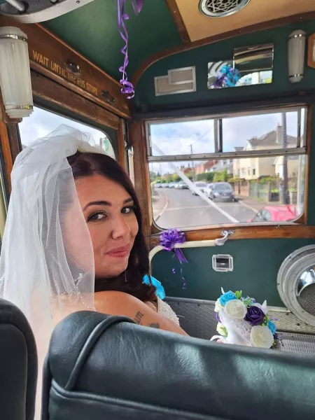 Laura, a young woman, smiles in a wedding dress from a vehicle.