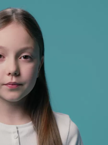 A young Caucasian girl stands against a blue backdrop wearing a white t-shirt