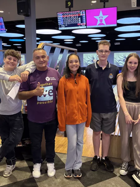 A group of young people and Young Epilepsy staff smile at a bowling alley.