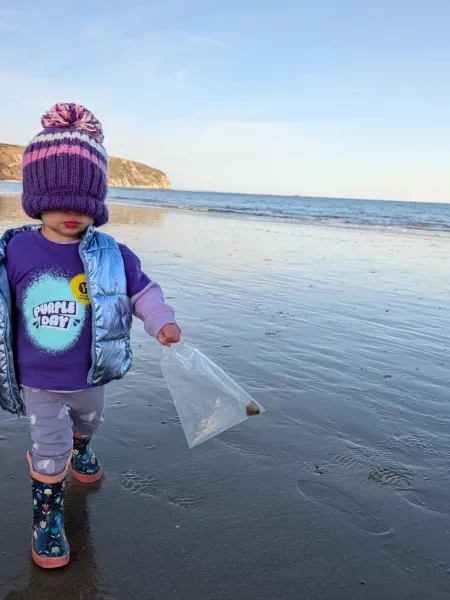 Young girl wearing a Young Epilepsy Purple Day t-shirt on a beach with a hat