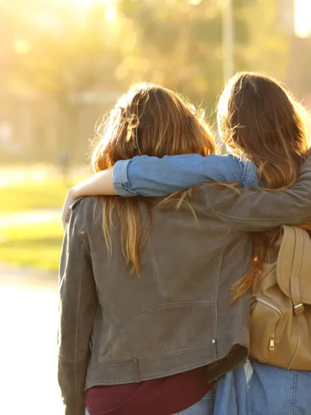 Two female friends stand arm in arm.