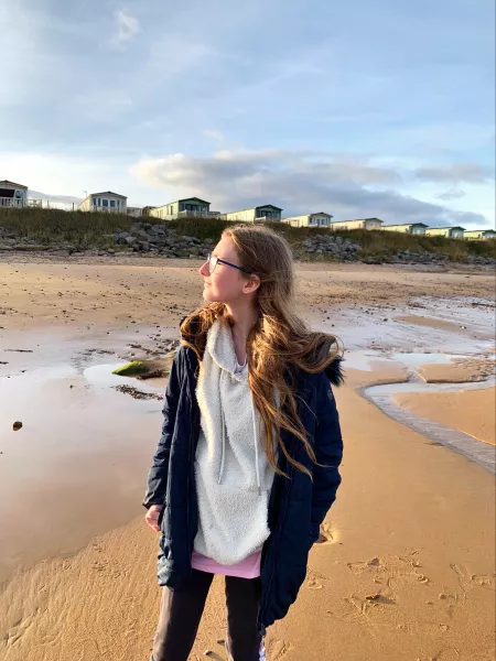 A young woman looks into the sun on a beach.
