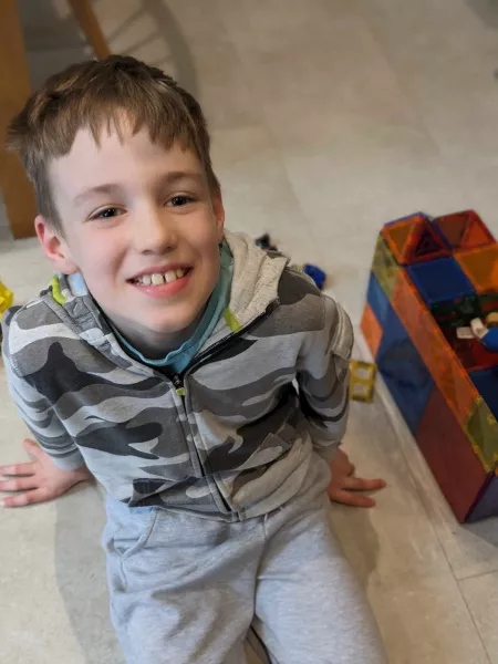A boy smiles beside his toy blocks.