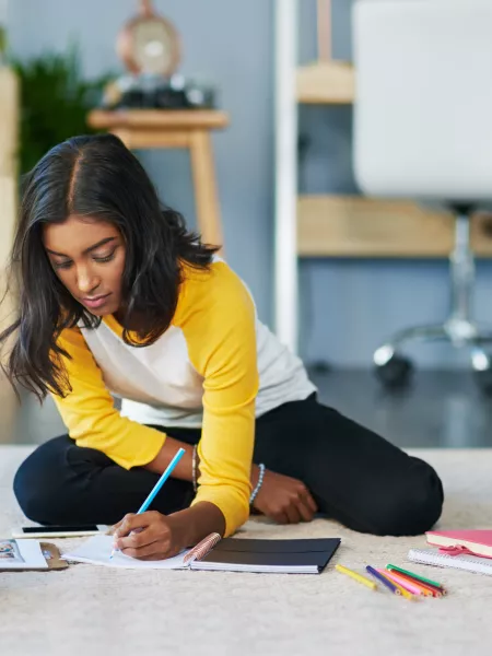 A teenager, sat on the floor, writes notes down in a diary.