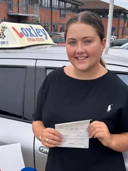 A young woman stands by a learner car, showing that she passed her driver's license.
