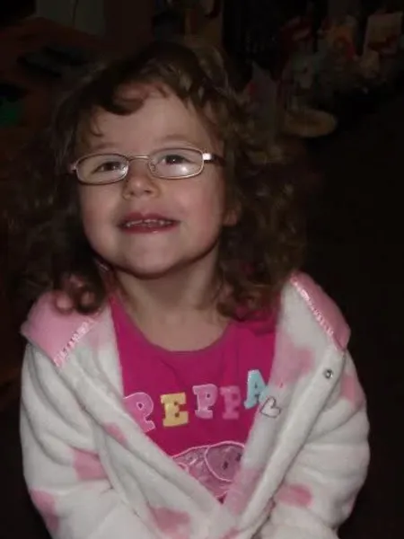 Young girl wearing glasses smiling to camera wearing pink pyjamas.