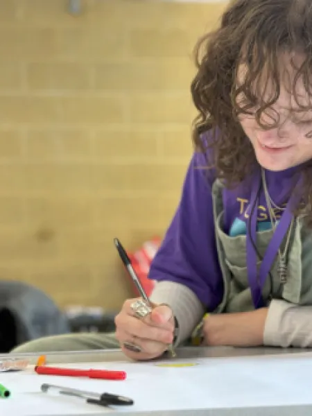 Young girl with a pen in hand writes on a piece of paper at a desk, smiling