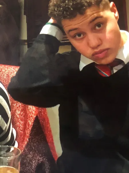 A young man in a school uniform touches his hair in a selfie.